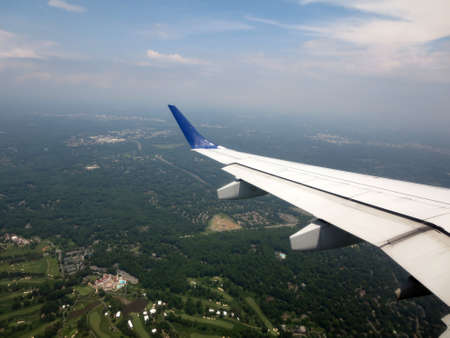 airplane wing as it flies into city with Golf course and forest visible in Washington DC area.