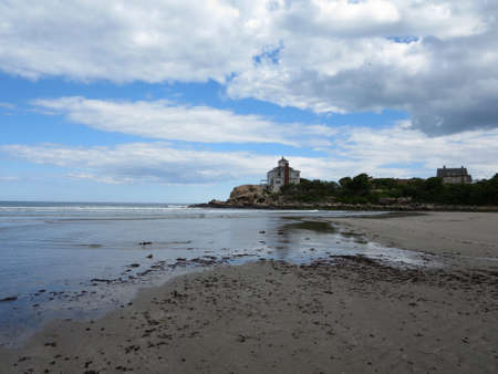 waves lap on beach with nice house on rocky hill in distance at Good Harbor Beach, Gloucester, Massachusetts. On a nice day.の写真素材