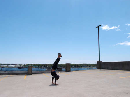 Man wearing a hoodie, pants, and slippers does Handstands on top of a parking garage the City of Portland Maine with Casco bay in the distance.の写真素材