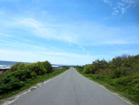 Peaks Island road way with granite rocky shoreline, trees and awesome sky in Maine.の写真素材