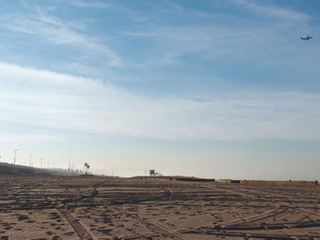 Tire tracks in the sand on an empty Dockweiler Beach State Park, Playa Del Rey in LA, California in the morning with plane flying in the air.の写真素材