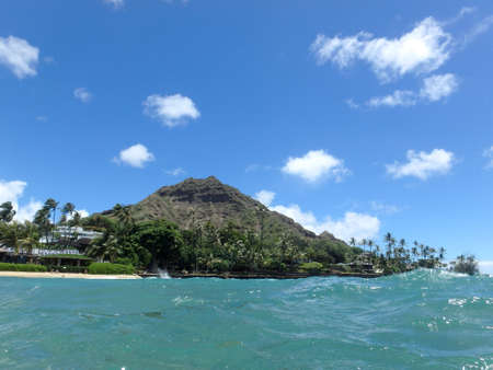 Beach and Makalei Beach Park with seawall, coconut trees, homes, and Diamond Head Crater in the distance on Oahu, Hawaii viewed from the water.の写真素材