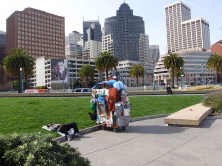 SAN FRANCISCO - FEBRUARY 18: Homeless man sleeps with homemade shopping carts filled with buckets, clothes, a chair and various other things along the Embarcadero with Downtown buildings in the background in San Francisco California, February 18, 2009 のeditorial素材