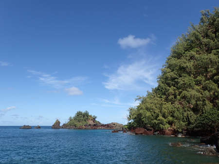 Red Rock cliff and islands covered with trees along the ocean Hana, Maui.の写真素材