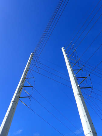 High Voltage Power Lines run through a large metal Utility pole in Oahu against a blue sky.