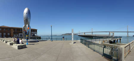 SAN FRANCISCO, CALIFORNIA - JUNE 23, 2011: Panoramic of the 40-foot Raygun Gothic Rocketship sculpture that adorns the San Francisco waterfront at the city's Pier 14 with people hanging out and Bay Bridge in the distance.のeditorial素材