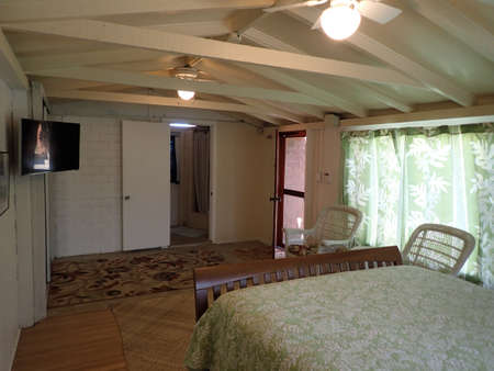 Inside Cottage Bedroom with Queen bed, Mounted HDTV, White Wicker chairs and bathroom.の写真素材