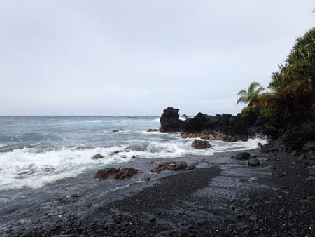 Waves break along Honomaele Black Sand Beach lined with coconut trees on Maui, Hawaii.の写真素材