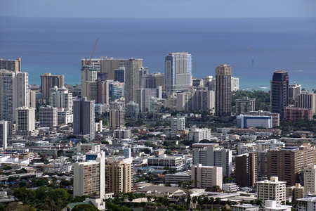 Honolulu cityscape, roads, buildings, skyscrapers, cranes, parks, and Pacific Ocean with clouds in the sky seen from up in the mountains on Oahu, Hawaii.の写真素材