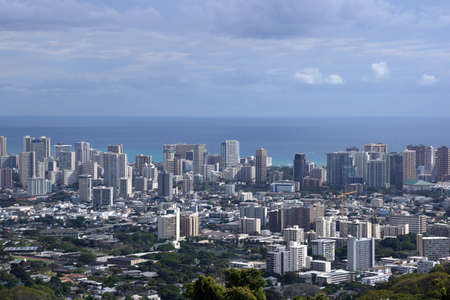 Honolulu cityscape, roads, buildings, skyscrapers, cranes, parks, and Pacific Ocean with clouds in the sky seen from up in the mountains on Oahu, Hawaii.の写真素材