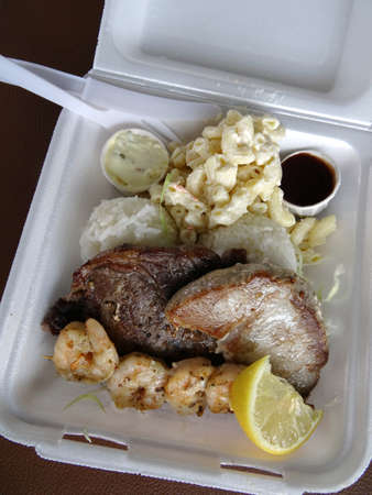 Surf & Turf Includes: Ahi, Steak, Shrimp, rice, and macaroni  salad with small cups of sauce, lemon in a styrofoam tray with plastic knife and fork.の写真素材