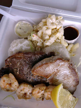 Surf & Turf Includes: Ahi, Steak, Shrimp, rice, and macaroni  salad with small cups of sauce, lemon in a styrofoam tray with plastic knife and fork.の写真素材