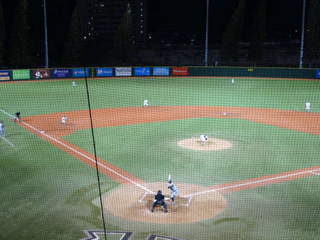 HONOLULU, HI - APRIL 17: CSUN Batter waits for incoming pitch leaving pitchers hand with catcher and umpire behind him during a night game seen through the net in the upper deck at UH Baseball Les Murakami Stadium in Manoa, Honolulu, Hawaii April 17, 2015のeditorial素材