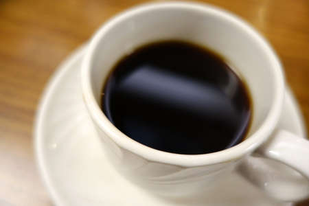 Close-up of Cafe cup of Coffee corner on plate sitting on a wood grain table.の写真素材