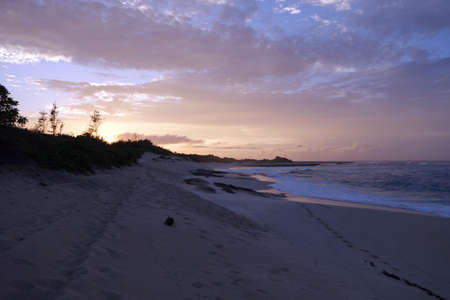Waves break and crash towards the Hanakailio Beach with dramatic blue-pink cloudy skyline at dusk with dragonfly in air on the North Shore of Oahu, Hawaii.の写真素材
