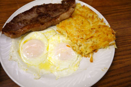 Steak ribs with two eggs over easy, Hash-brown potatoes and on a plate on table.の写真素材