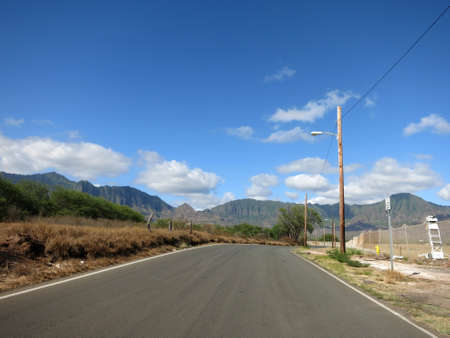 Long empty road in Maili Valley next to Naval Magazine and mountains in the distance on Oahu, Hawaii.の写真素材