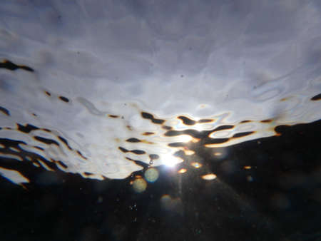 Sun light underwater with wave ripples, air bubbles, and particles of sand.の写真素材