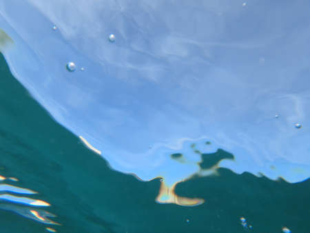 Sky light underwater with wave ripples, air bubbles, and particles of sand.の写真素材
