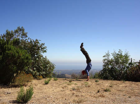 Man wearing long sleeve shirt, long pants, hat and shoes Handstands in the high mountains of Santa...