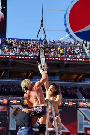 SANTA CLARA - MARCH 29: Dolph Ziggler and Daniel Bryan reaches for the Intercontinental championship belt as it hangs in the air with Dean Ambrose climbing towards them during ladder match at Wrestlemania 31 with crowd in the distance at the Levi's Stadiuのeditorial素材