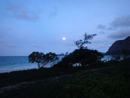 Gentle wave lap on Waimanalo Beach with full moon over Rabbit island on a nice evening Oahu, Hawaii.の写真素材