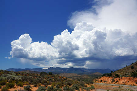 A Road winds Through a Desert in Utah and Blue cloudy Sky and mountains in the distance.の写真素材