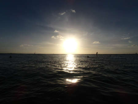 dramatic Sunset on waters of Kaimana Beach over the ocean with people in water and paddleboarders in the water on Oahu, Hawaii.の写真素材