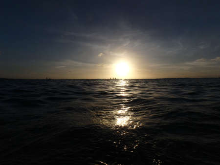 Dramatic Sunset on waters of Kaimana Beach over the ocean with boats and canoes on the water on Oahu, Hawaii.の写真素材