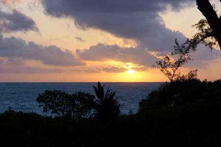 Early Morning Sunrise through the trees over an island and ocean on Waimanalo Beach on Oahu, Hawaii with clouds hanging in the air.の写真素材