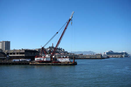 SAN FRANCISCO - OCTOBER 11:  Crane on barge does Pier repair work with Coit Tower on top Telegraph hill and Cruise ship in the distance in San Francisco, California.  October 11, 2015.のeditorial素材