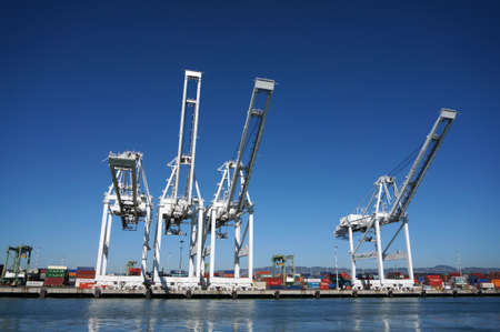 OAKLAND - OCTOBER 12: Row of Cargo Cranes tower over shoreline in Oakland Harbor on a nice day with Oakland and surrounding hills in the distance. The fourth busiest container port in the country, it's a major economic engine in the San Francisco Bay Areaのeditorial素材