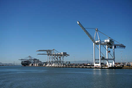 OAKLAND - OCTOBER 12: Shipping Cargo Boats line up in harbor under giants unloading cranes in Oakland Harbor and San Francisco in the distance.  Oakland California on October 12, 2015.のeditorial素材