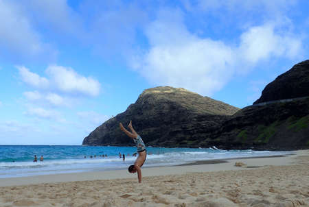 Man Handstanding on Makapuu beach as wave crash on the South east Shore of Oahu, Hawaii.の写真素材