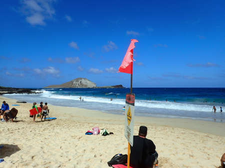 OAHU - FEBRUARY 14: People play at the beach with strong current sign on beach and view of islands Rabbit and Rock on a clear day at Makapuu Beach Park, Oahu, Hawaii.   February 14, 2016.のeditorial素材