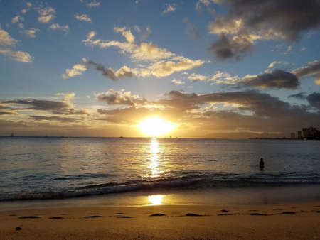 dramatic lighting as Sunsets over the ocean with Waianae mountains in the distance with light reflecting on ocean and illuminating the sky with boats sailing on the water off Waikiki on Oahu, Hawaii.の写真素材