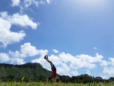 Man Handstanding in Kapiolani Park at during day with Diamond Head and clouds in the distance on...