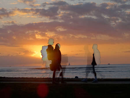 Waikiki - January 16, 2016:  Sunset dropping behind the ocean on Kaimana Beach and images of people walking by with boats on the water on Oahu, Hawaii.のeditorial素材