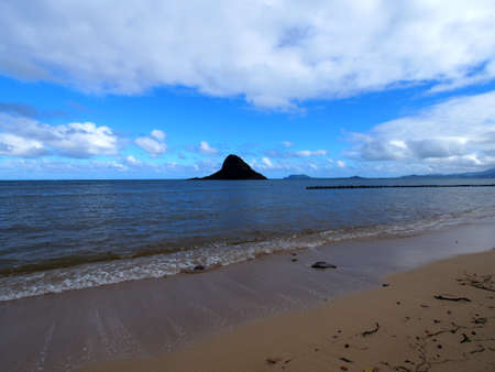 Beach with MokoliÊ»i isalnd or Chinaman's Hat in the distance, which is a 12.5-acre (5.1 ha), 206-foot-tall (63 m) basalt island 1â3 miles (0.54 km) offshore of Kualoa Point, Oahu, in KÄne'ohe Bay, Hawaii.の写真素材