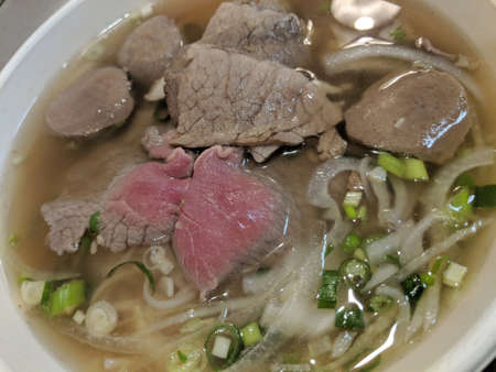 Close-up of Pho (Vietnamese Rice Noodle Soup) with Beef, Meat Ball, onions, and chives.