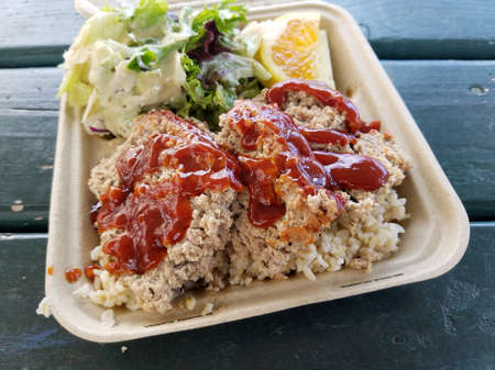 Turkey Meatloaf Plate Lunch with Brown rice, salad, and orange slice on green table.の写真素材