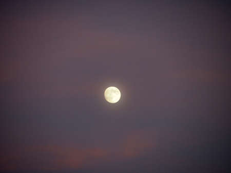 Almost full Moon in purple sky with a few clouds at dusk.の写真素材