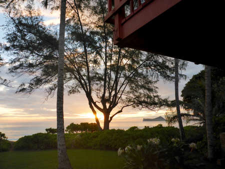 Sunrise over ocean by Manana Island by Rabbit Island with Red House Balcony through the trees on Waimanalo Beach on Oahu, Hawaii.の写真素材