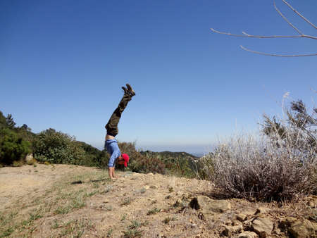 Man wearing long sleeve shirt, long pants, hat and shoes Handstands in the high mountains of Santa Barbara, California.の写真素材