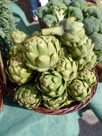 Pile of Artichoke and broccoli in baskets on display at a farmers market in San Francisco, CA.の写真素材