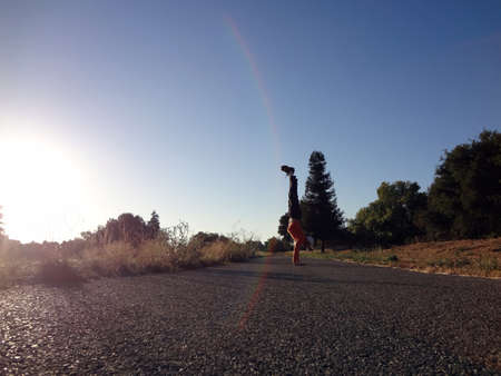 Man Handstand along path with lens flare and trees of a park around him in San Jose, California.