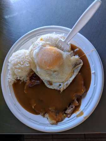 Corned Beef Hash With gravy, over easy egg, and rice on a plastic plate on a table.の写真素材