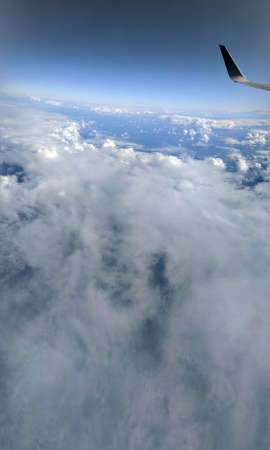 Aerial high in the sky, shot from above the clouds, with the wing of a commercial jet plane that...