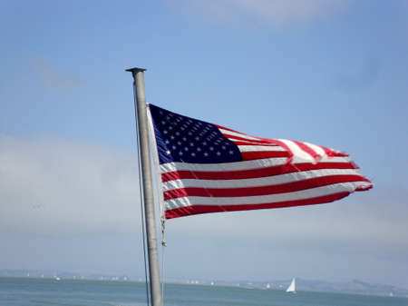 tattered USA flag waves in the wind on the back of a ferry with San Francisco Bay in the background.