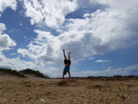 Man does Handstand on beach at Kuilima Point with clouds in the sky on the North Shore of Oahu,...